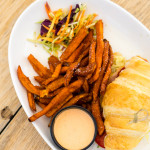 Peameal bacon and fried egg sandwich with O&B artisan butter croissant, lettuce, tomato, avocado mayo, sweet potato fries